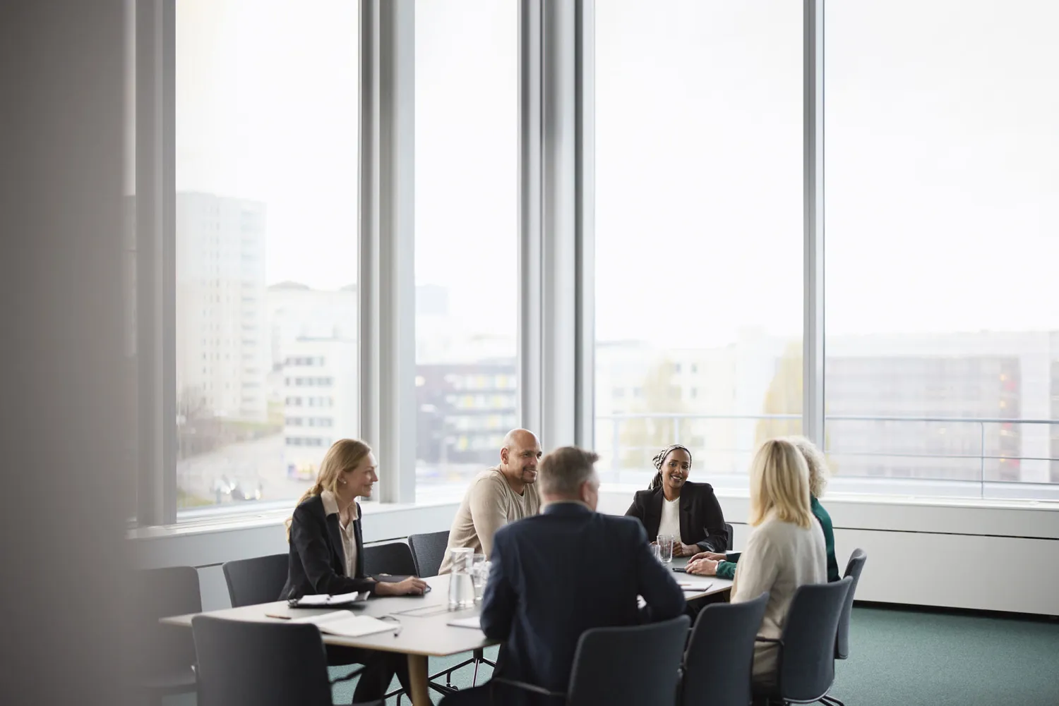 Work colleagues talk together in a meeting room with large windows