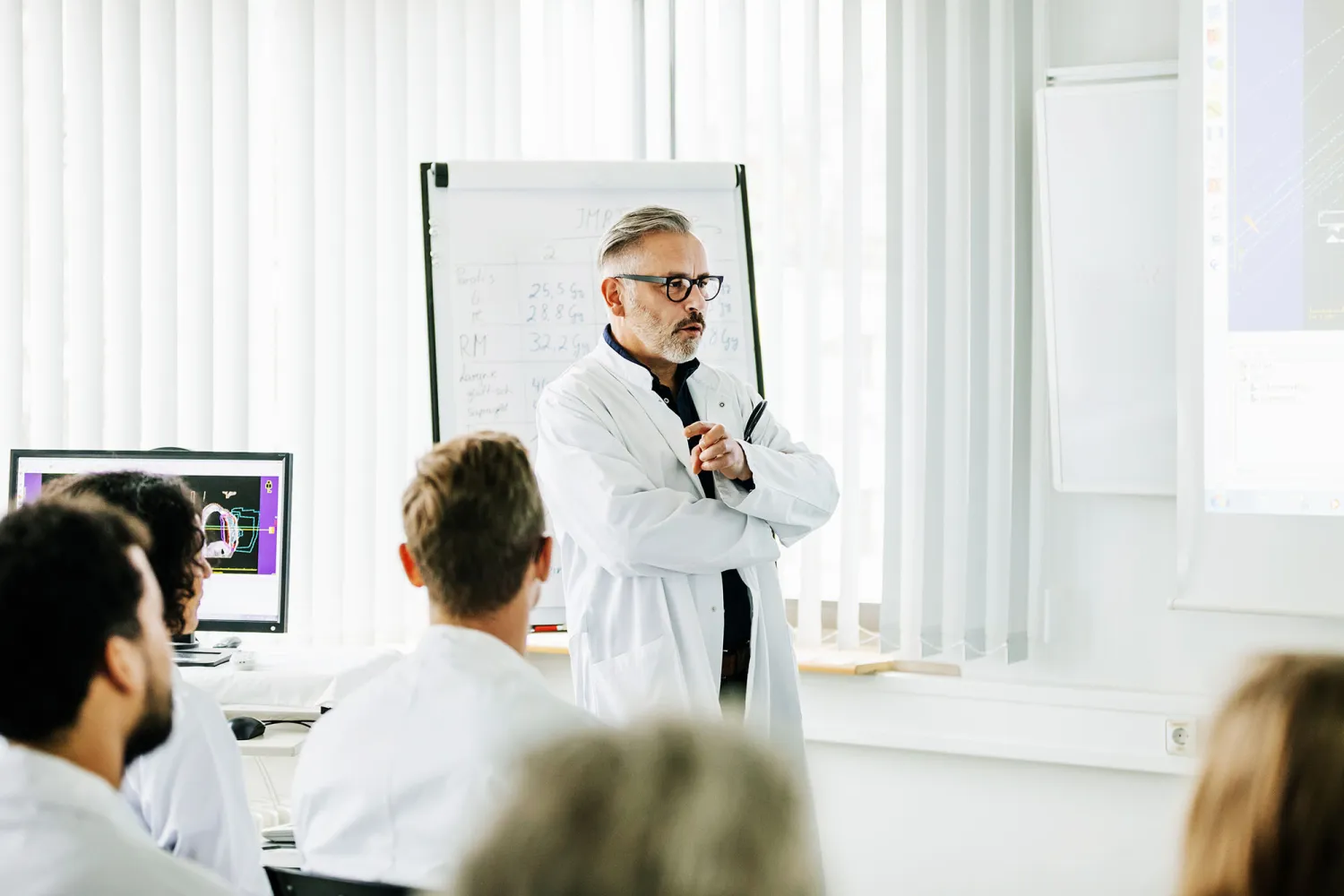 A lab scientist runs a meeting with his team around a whiteboard